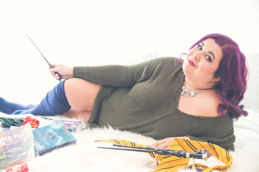 Woman with long purple hair wearing a cozy sweater and knee socks lounges on a furry rug holding a magic wand.