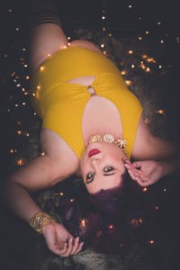 Woman in a yellow dress lays on the ground surrounded by soft fairy lights around her and in her hair.