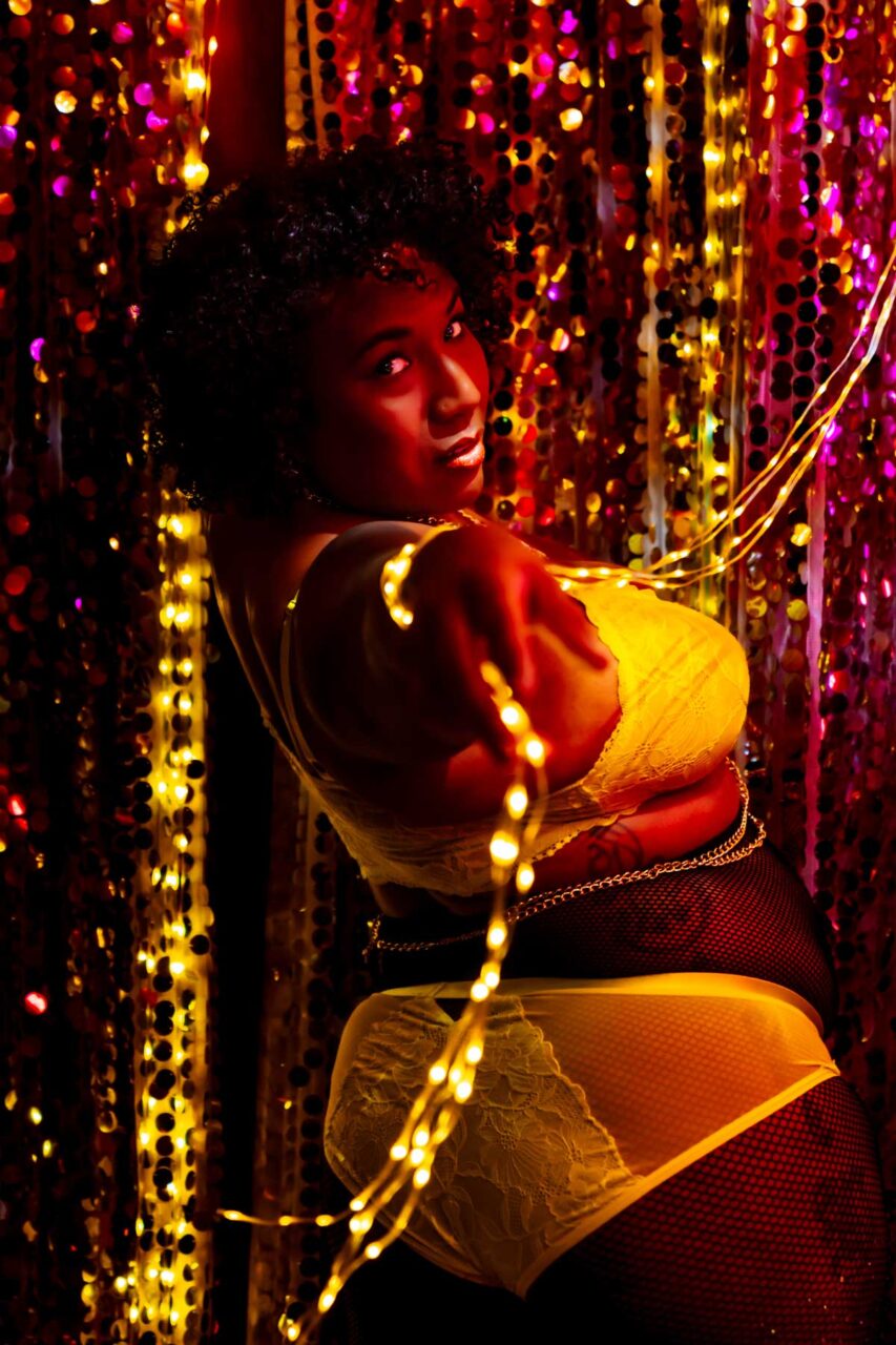 Plus size black woman in yellow lingerie posing for boudoir session in neon lights
